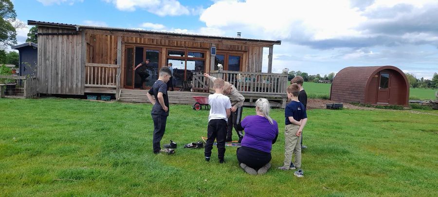 A group gathered on the grass with a craft activity outside the cabin